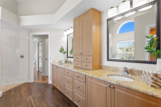 full bathroom featuring a sink, wood finished floors, double vanity, and a tile shower