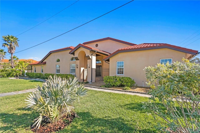 mediterranean / spanish home with a front yard, a tiled roof, and stucco siding