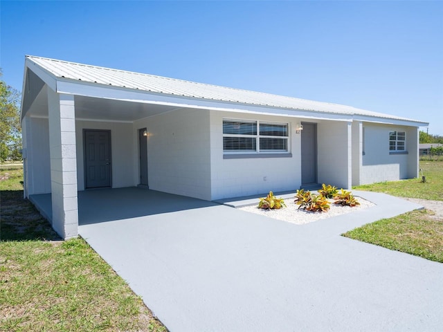 single story home with metal roof, an attached carport, concrete block siding, and concrete driveway