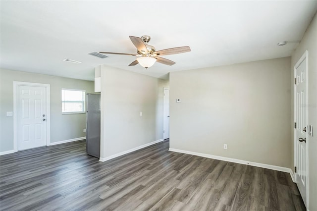 empty room featuring a ceiling fan, visible vents, dark wood-style floors, and baseboards