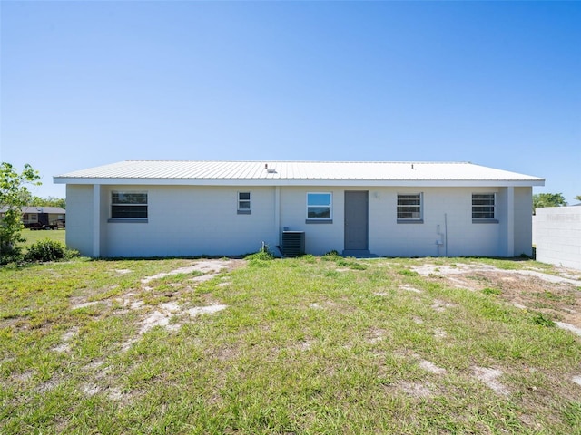 back of house featuring concrete block siding, central AC unit, a lawn, and metal roof