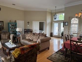 living room featuring wood finished floors, a high ceiling, ornamental molding, french doors, and a notable chandelier