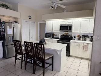 kitchen with a breakfast bar, light countertops, light tile patterned floors, stainless steel appliances, and white cabinetry