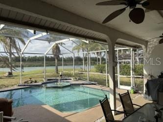 outdoor pool featuring glass enclosure, a water view, a ceiling fan, and a patio area