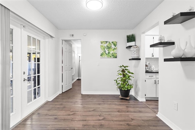 corridor featuring visible vents, dark wood-style floors, baseboards, and a textured ceiling