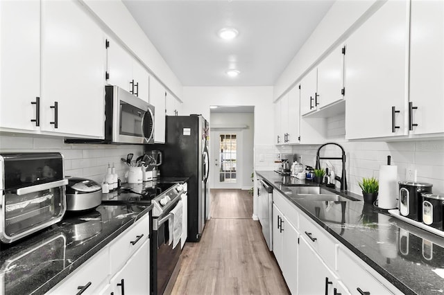 kitchen featuring light wood finished floors, dark stone counters, appliances with stainless steel finishes, white cabinetry, and a sink