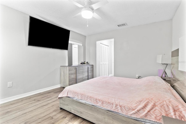 bedroom featuring wood finished floors, visible vents, baseboards, ceiling fan, and a textured ceiling