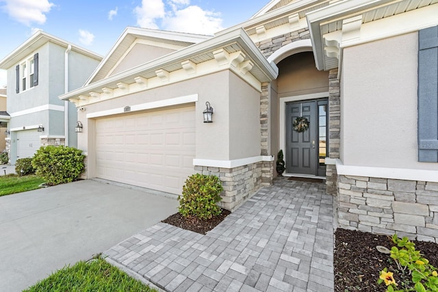 property entrance with stucco siding, stone siding, a garage, and driveway