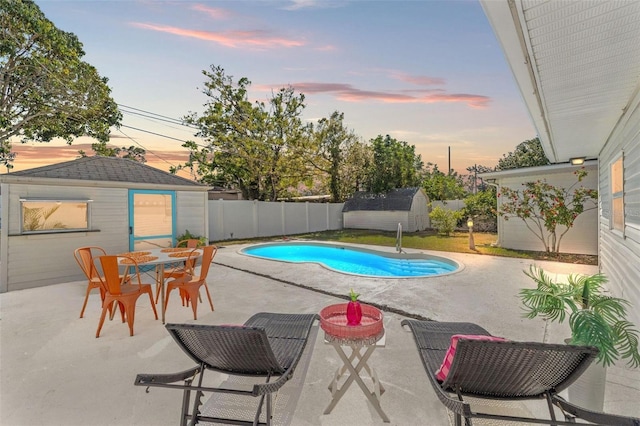 pool at dusk featuring a fenced backyard, a patio, and an outdoor structure