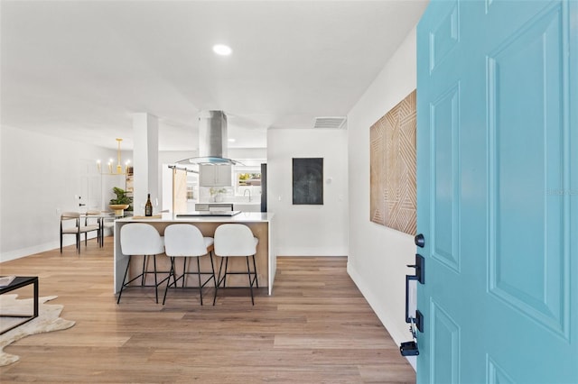 kitchen with visible vents, a breakfast bar, a peninsula, island range hood, and light wood finished floors