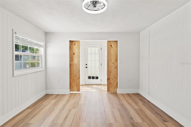 spare room with baseboards, light wood-type flooring, and a textured ceiling