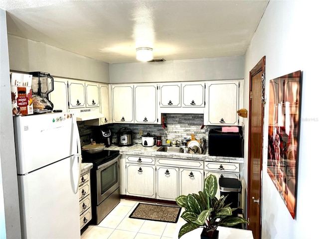 kitchen with under cabinet range hood, stainless steel electric stove, light countertops, freestanding refrigerator, and a sink