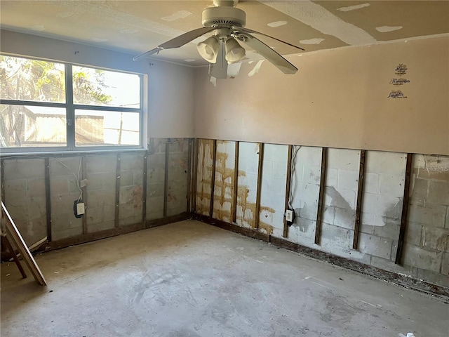 spare room featuring concrete block wall, ceiling fan, and unfinished concrete floors