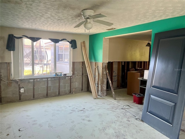 interior space featuring visible vents, a textured ceiling, concrete block wall, and a ceiling fan