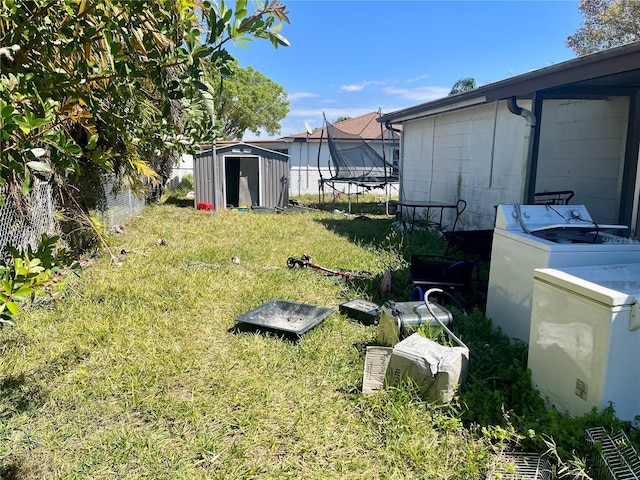 view of yard featuring washer / clothes dryer, a storage shed, a trampoline, and an outdoor structure