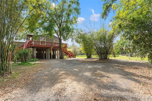 view of yard featuring stairs, a wooden deck, a carport, and dirt driveway