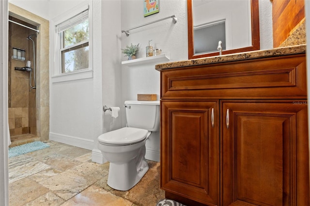 full bath with vanity, baseboards, a tile shower, stone finish floor, and toilet