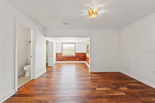 interior space with wood finished floors, a wainscoted wall, baseboards, visible vents, and a textured ceiling