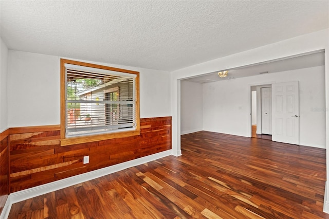 unfurnished room with a textured ceiling, wood finished floors, wood walls, and wainscoting