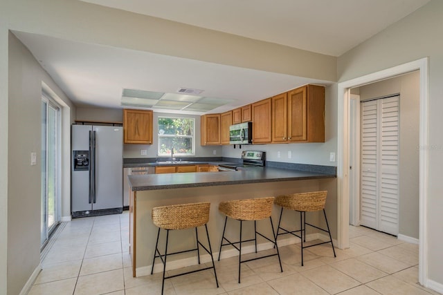 kitchen featuring dark countertops, brown cabinetry, a peninsula, and stainless steel appliances