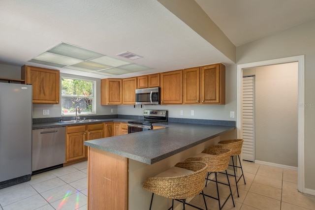 kitchen with dark countertops, visible vents, brown cabinets, stainless steel appliances, and a sink