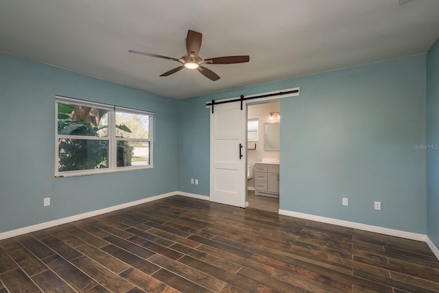 unfurnished bedroom featuring a barn door, baseboards, dark wood-type flooring, and ensuite bathroom