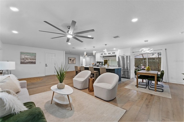 living area featuring visible vents, baseboards, light wood finished floors, and ceiling fan