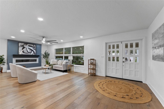 living room featuring baseboards, hardwood / wood-style floors, recessed lighting, a glass covered fireplace, and a textured ceiling