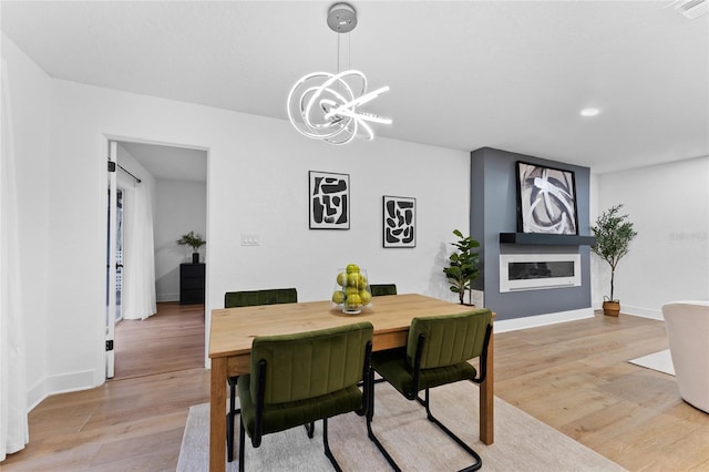 dining area featuring visible vents, baseboards, an inviting chandelier, light wood-style floors, and a glass covered fireplace