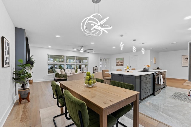 dining space with recessed lighting, ceiling fan with notable chandelier, light wood-style floors, and baseboards