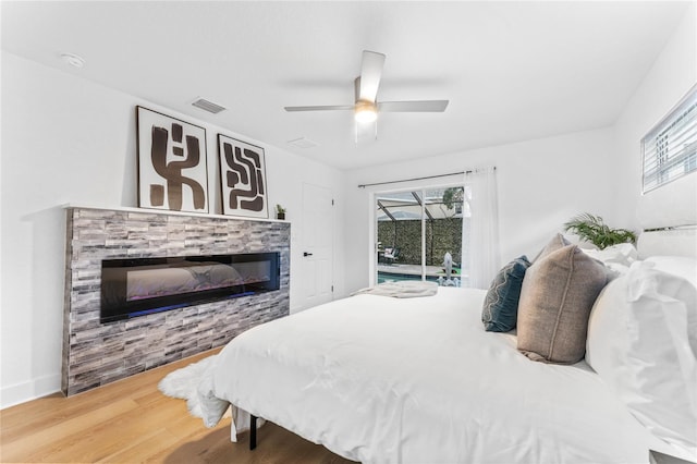 bedroom featuring visible vents, a sunroom, wood finished floors, a glass covered fireplace, and access to outside