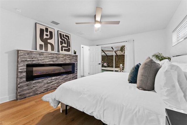 bedroom featuring wood finished floors, visible vents, multiple windows, and a glass covered fireplace