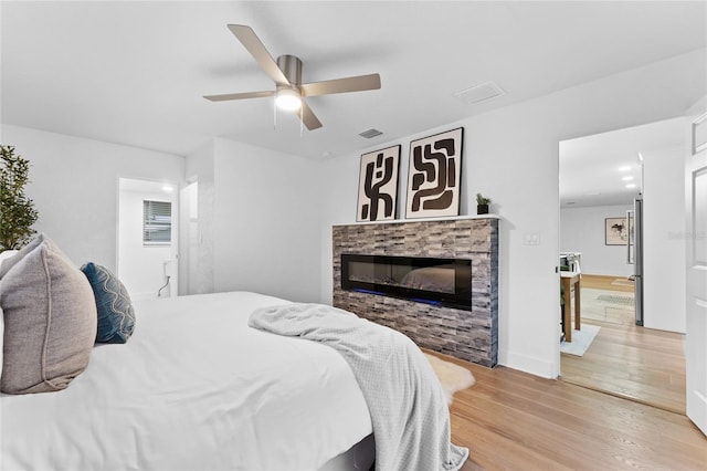 bedroom with visible vents, light wood-style floors, a glass covered fireplace, and a ceiling fan