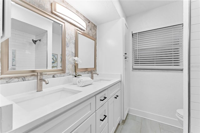 bathroom with a tile shower, double vanity, baseboards, and a sink