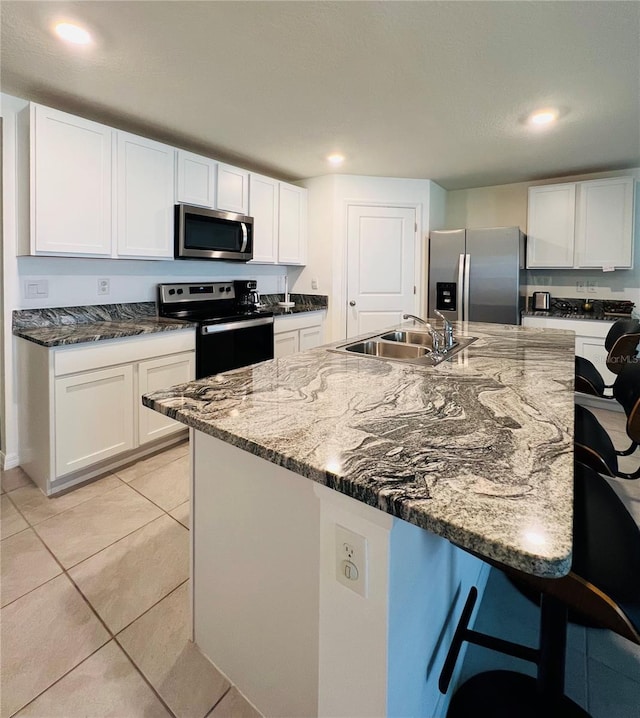 kitchen featuring a kitchen bar, light tile patterned floors, stainless steel appliances, white cabinetry, and a sink