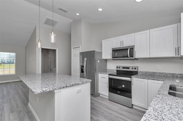 kitchen with visible vents, a kitchen island, light stone counters, appliances with stainless steel finishes, and white cabinetry