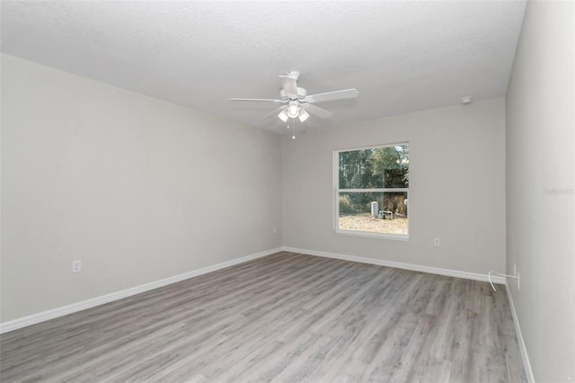 spare room featuring a textured ceiling, baseboards, light wood-style floors, and a ceiling fan