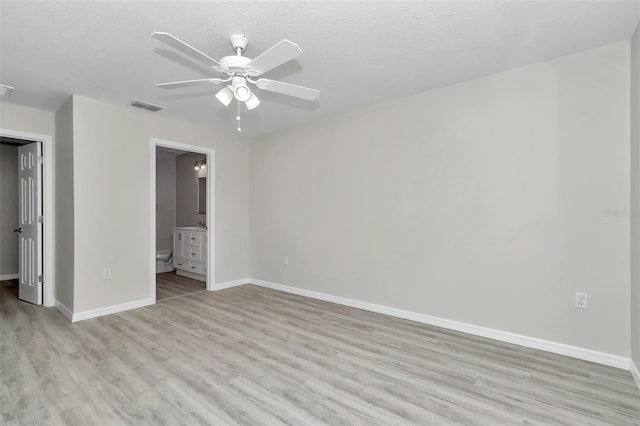 unfurnished bedroom featuring baseboards, visible vents, light wood finished floors, ceiling fan, and ensuite bathroom