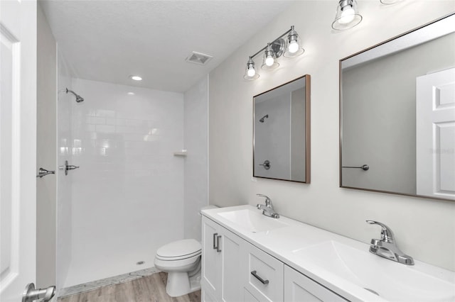 bathroom featuring visible vents, tiled shower, toilet, and a sink