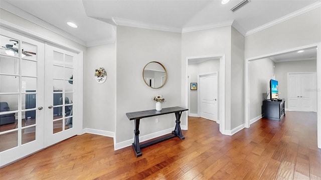 hallway with visible vents, wood-type flooring, baseboards, and ornamental molding