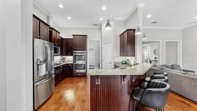 kitchen featuring a sink, a kitchen breakfast bar, open floor plan, a peninsula, and appliances with stainless steel finishes