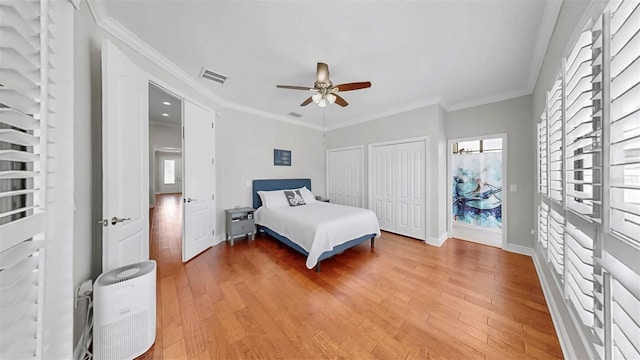 bedroom featuring visible vents, baseboards, multiple closets, ornamental molding, and light wood-style floors