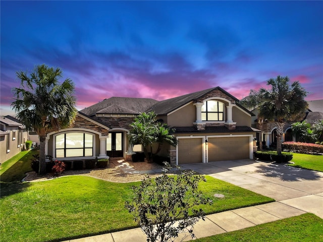 view of front of home featuring driveway, a yard, an attached garage, stucco siding, and stone siding