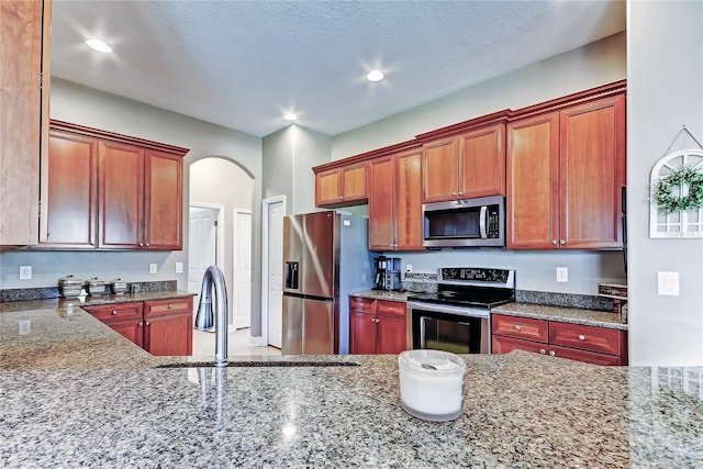 kitchen with recessed lighting, arched walkways, stone countertops, stainless steel appliances, and a sink