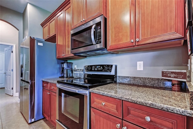 kitchen featuring stone counters, light tile patterned floors, arched walkways, and appliances with stainless steel finishes