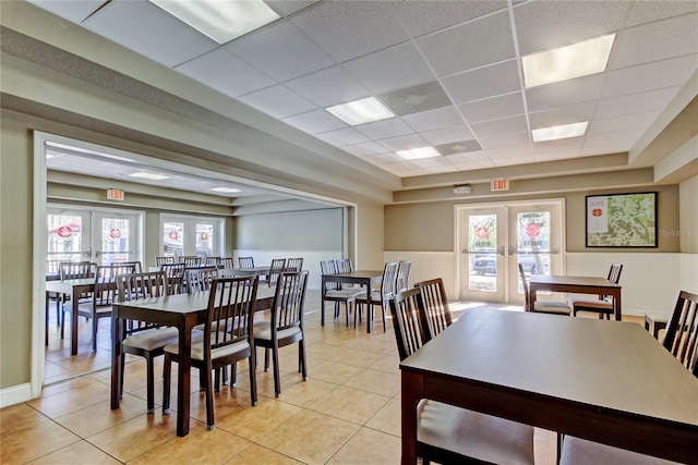 dining space featuring light tile patterned floors, a drop ceiling, french doors, and baseboards