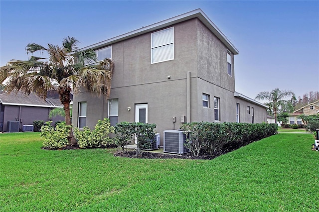 rear view of property featuring central AC unit, a lawn, and stucco siding