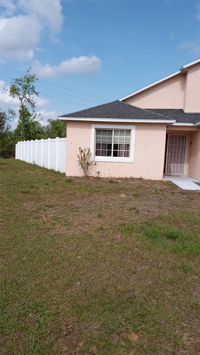 view of side of home with fence, a lawn, and stucco siding