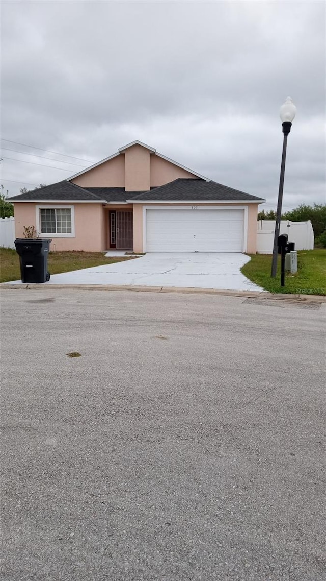 ranch-style home featuring driveway, stucco siding, an attached garage, and fence