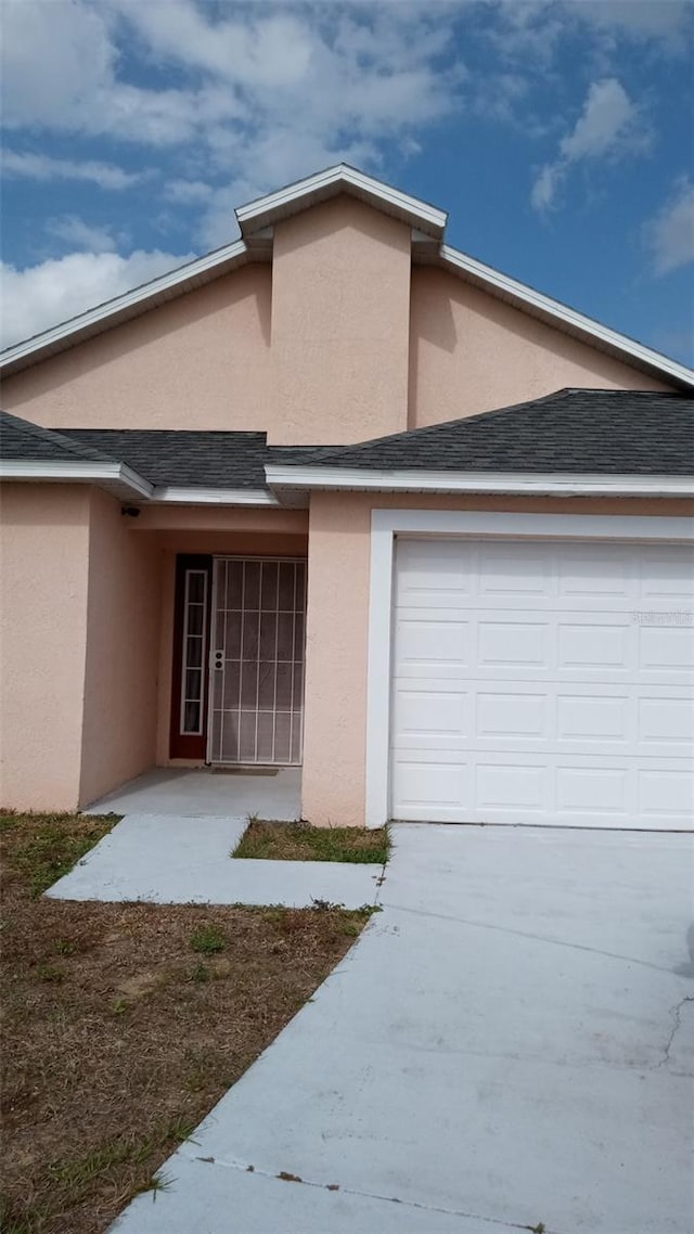 view of front of home with stucco siding, concrete driveway, a shingled roof, and a garage